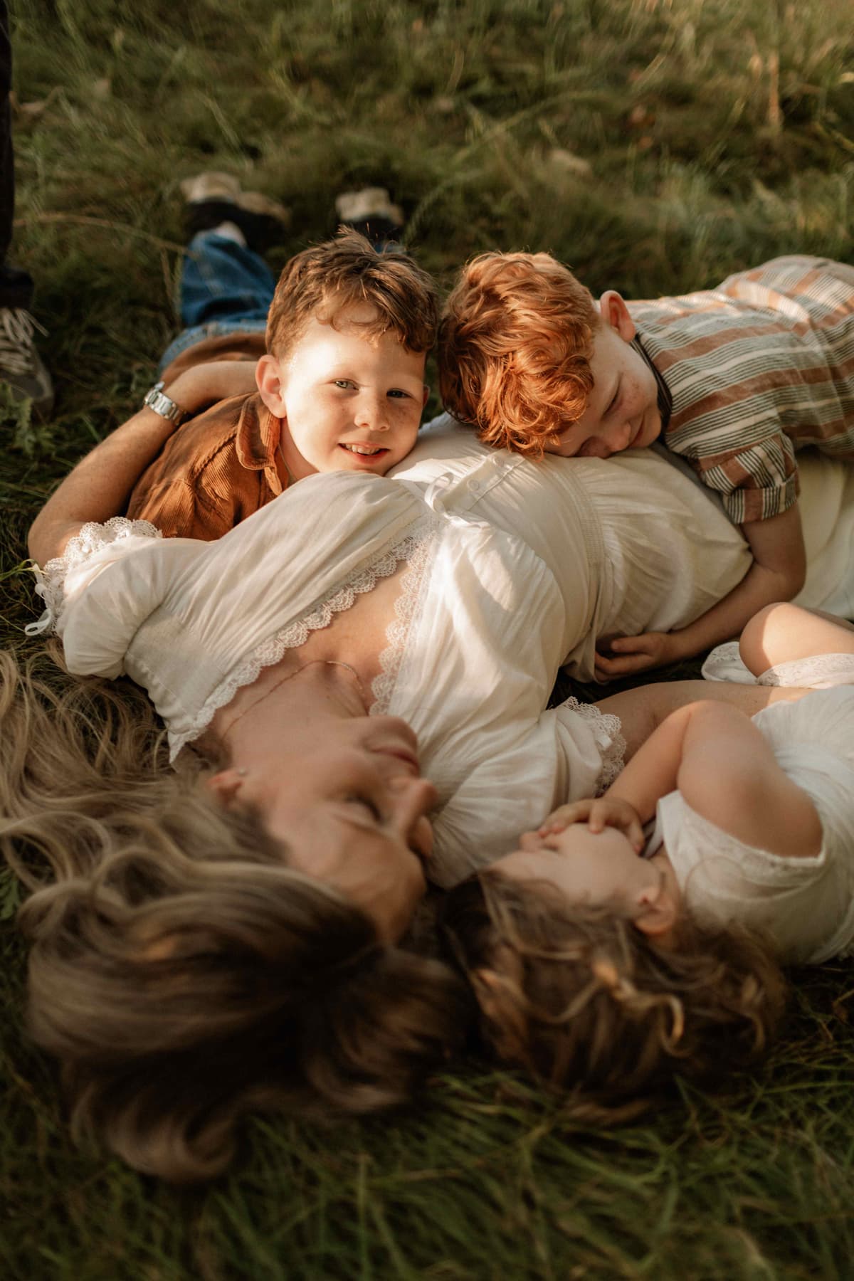 Mother lying in a golden sunlit field with her two children resting on her, all smiling and laughing